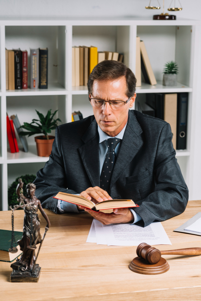 mature-male-lawyer-reading-book-with-gavel-justice-statue-wooden-table